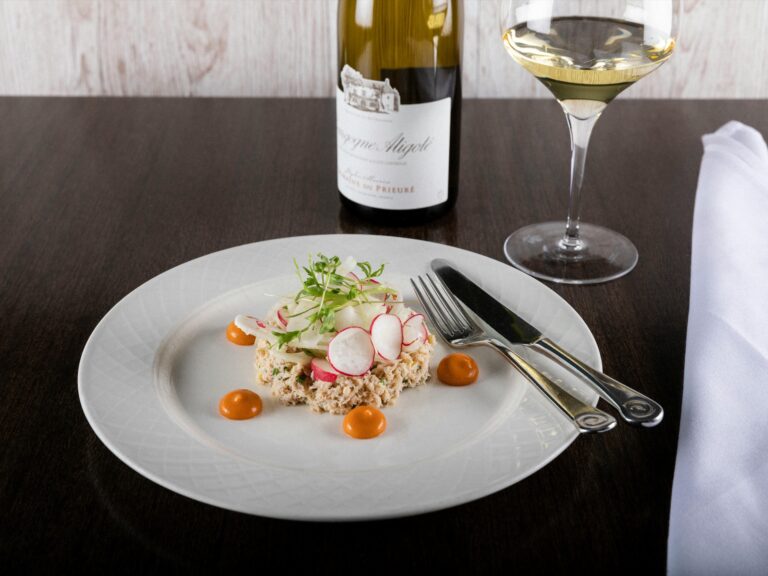 A plated starter with radish and microherbs, served with a glass of white wine and the bottle behind, Captain's Club Hotel & Spa