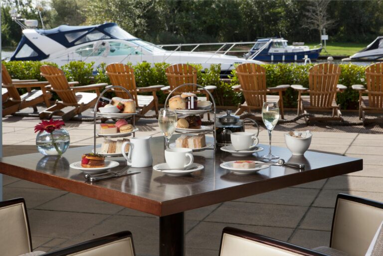 Afternoon tea stands on a terrace table, with wooden deckchairs and motor boats moored alongside, Captain's Club Hotel & Spa