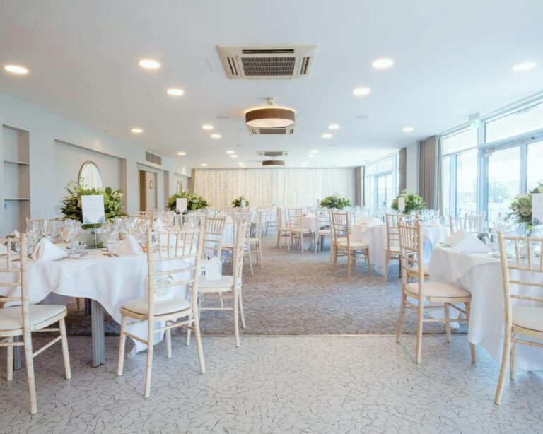 The Waterside Suite laid with round tables, white linen and limewash chairs, with windows along the river side, Captain's Club Hotel & Spa