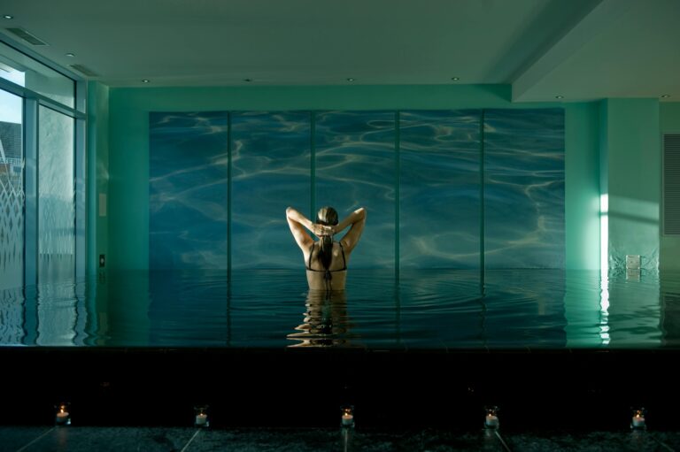 The spa hydrotherapy pool against a wall of rippled blue glass, a bather seen from behind, Captain's Club Hotel & Spa