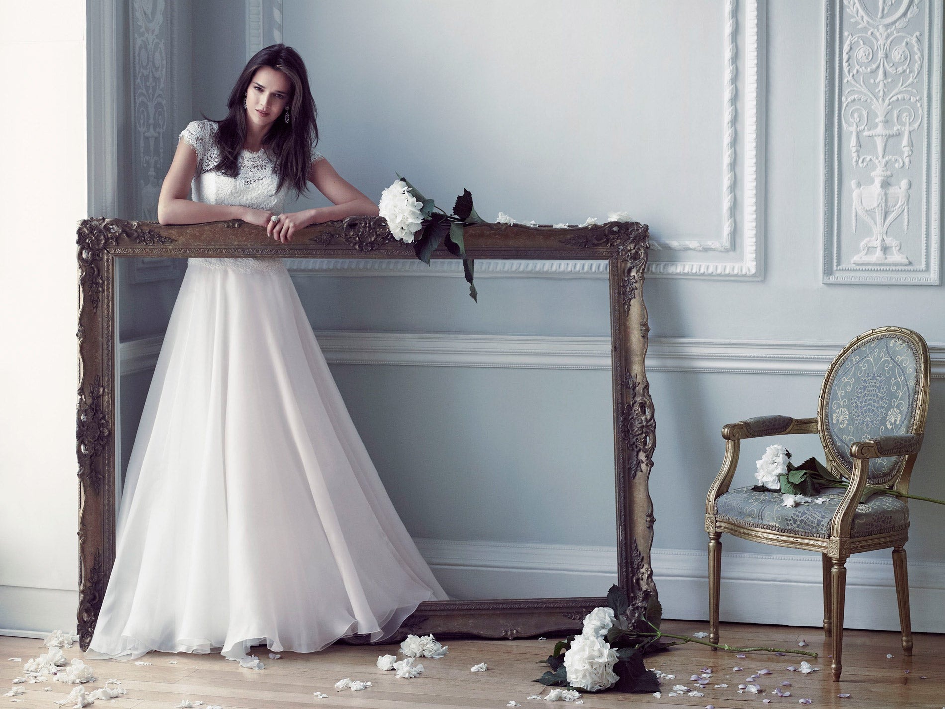A long skirted gown and bouquet set beside a gilded frame in a pale room, Caroline Castigliano