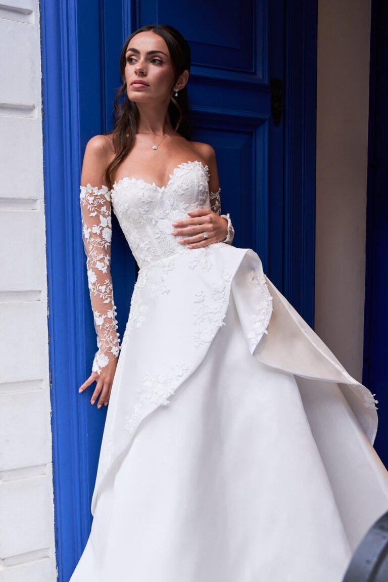 The Eternal Rose gown with lace sleeve and draped skirt beside a blue door, Caroline Castigliano