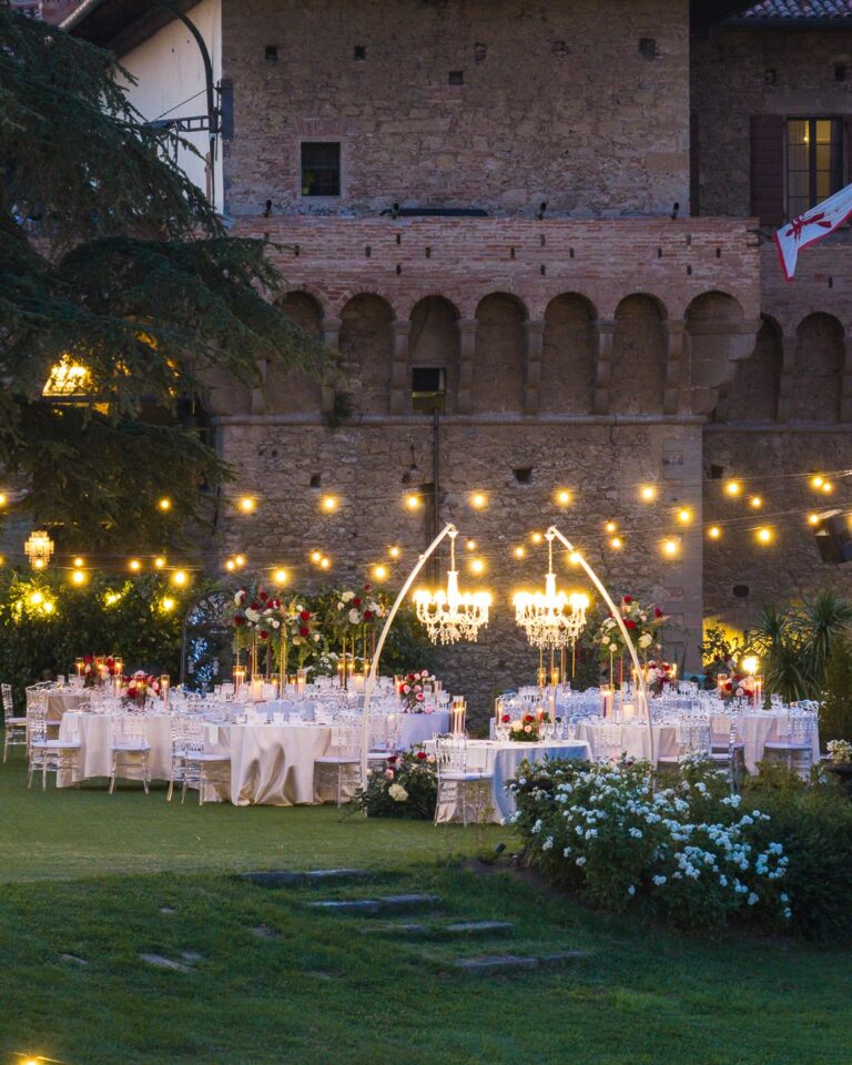 Tables laid under chandeliers below the castle wall in the evening, Castello del Capitano delle Artiglierie