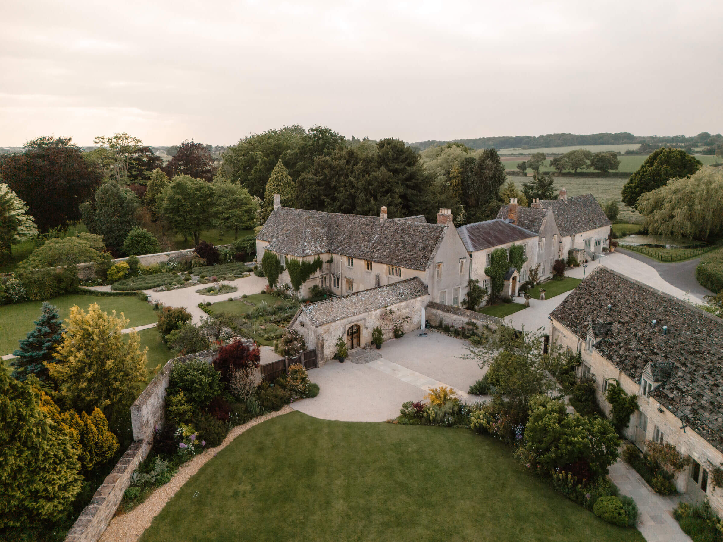 Aerial view of the house, the stone barns around the courtyard and the lawn, with Oxfordshire farmland beyond, Caswell House