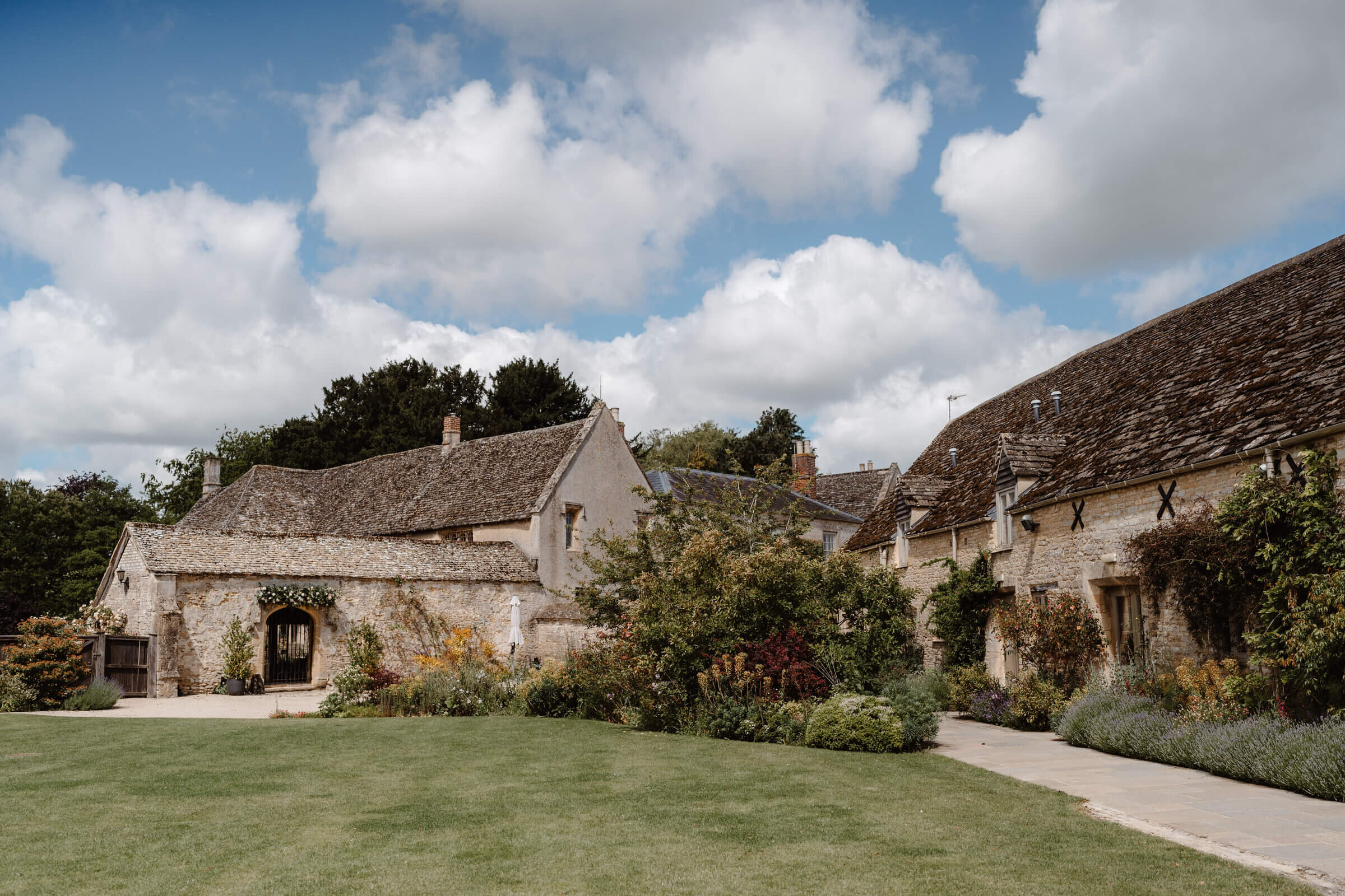 The stone-slated barns seen across the lawn, with planted borders along the walls, Caswell House