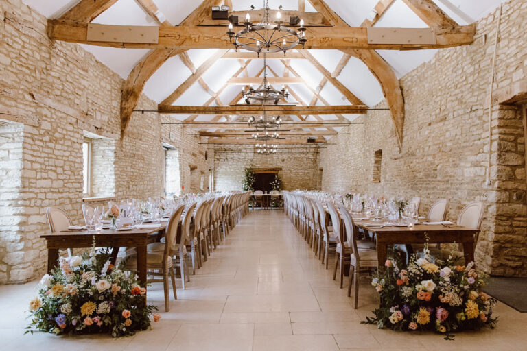 Two long tables laid for dinner down the length of the barn, with floral arrangements at each end, Caswell House