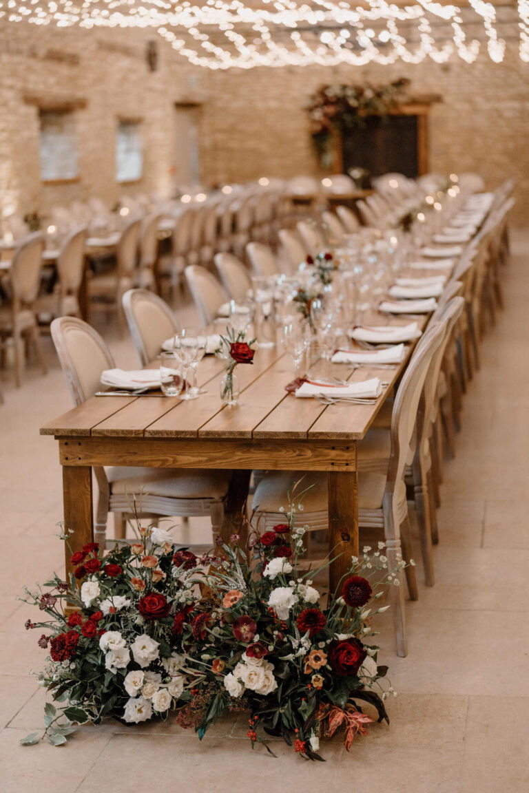 A wooden banqueting table laid for dinner, with a meadow-style flower arrangement at its end, Caswell House