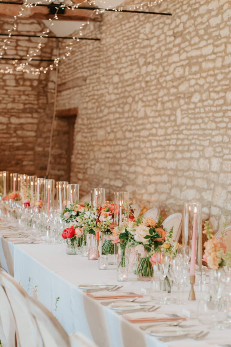 A table dressed with pink and peach flowers and tall candles against the barn's stone wall, Caswell House