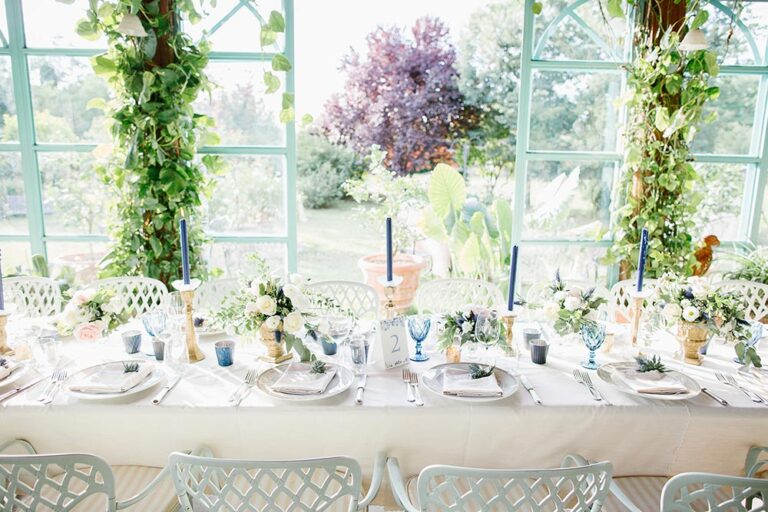 Dinner tables in a glass-walled garden room, Caterina Weddings