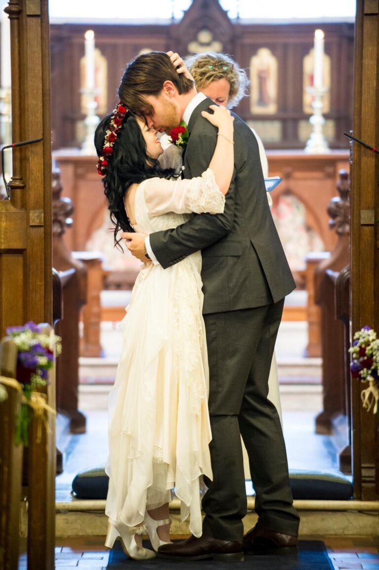 A couple kissing at a church altar, the bride in a cream layered gown, Catherine Blades Couture
