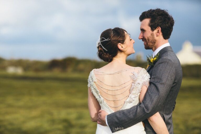 A bride in a gown with a beaded and chained back detail, embraced by her groom, Catherine Blades Couture