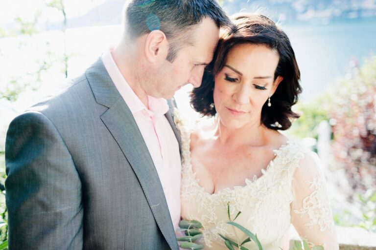A couple resting foreheads together, the bride in a gown with sheer lace sleeves, Catherine Blades Couture