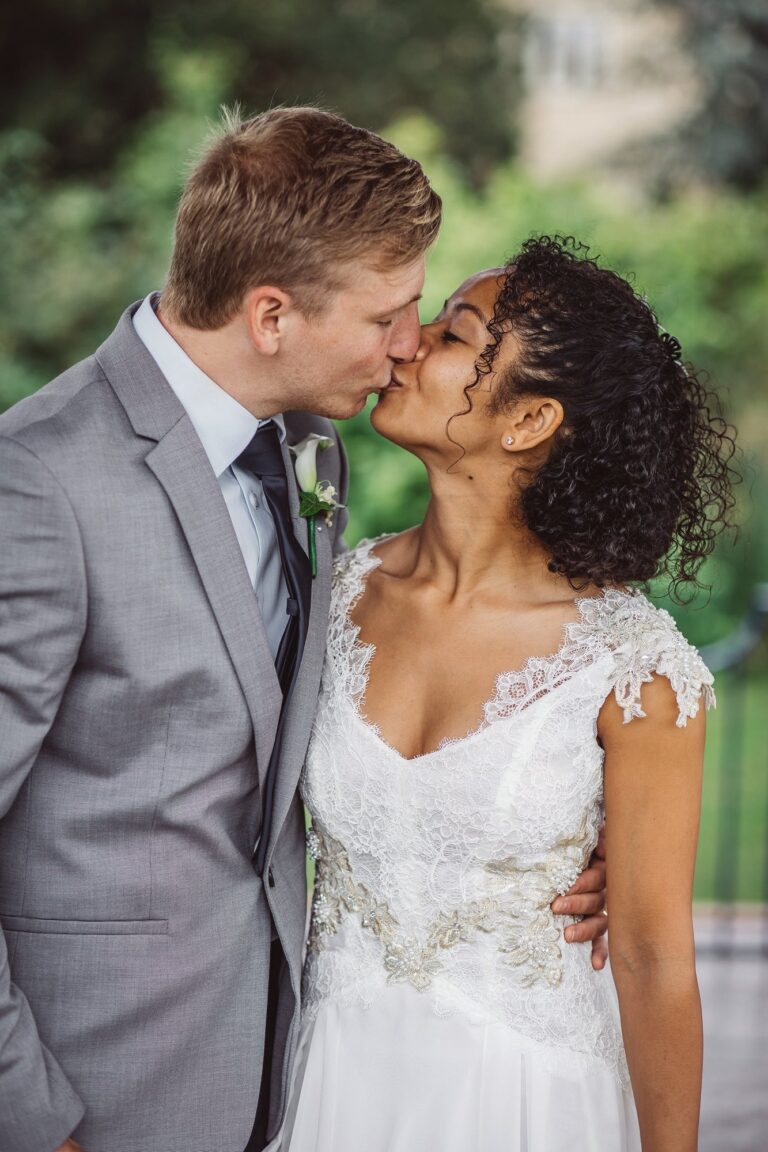 A couple kissing, the bride in a gown with beaded lace cap sleeves, Catherine Blades Couture