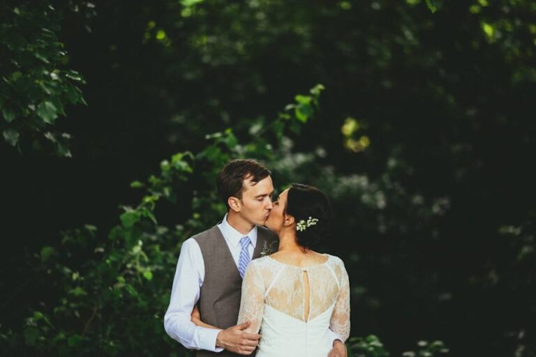 A couple kissing in a dark woodland, the bride in a lace-backed ivory gown, Catherine Blades Couture