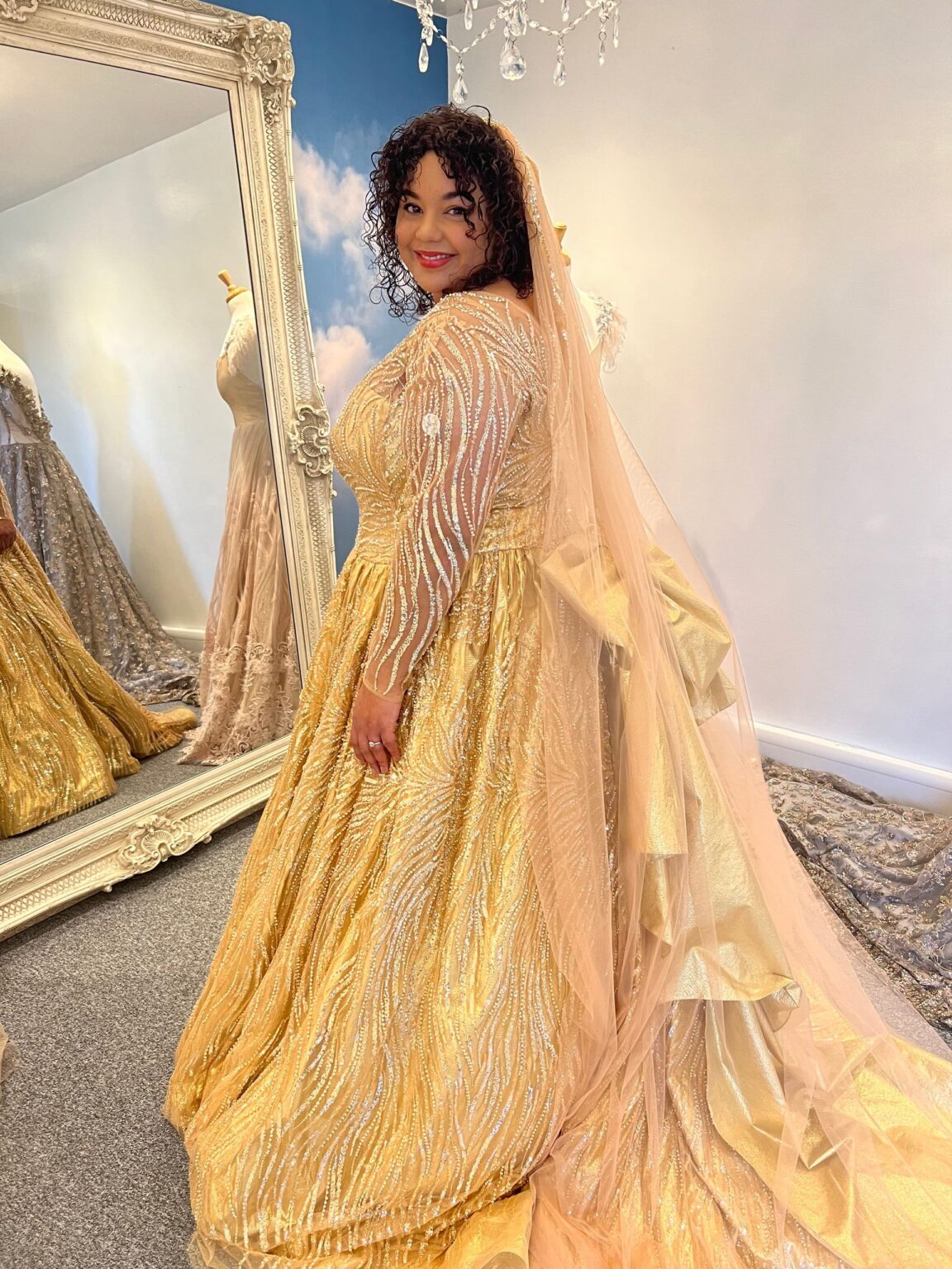 A client in a gold embellished gown with a long veil in the studio mirror room