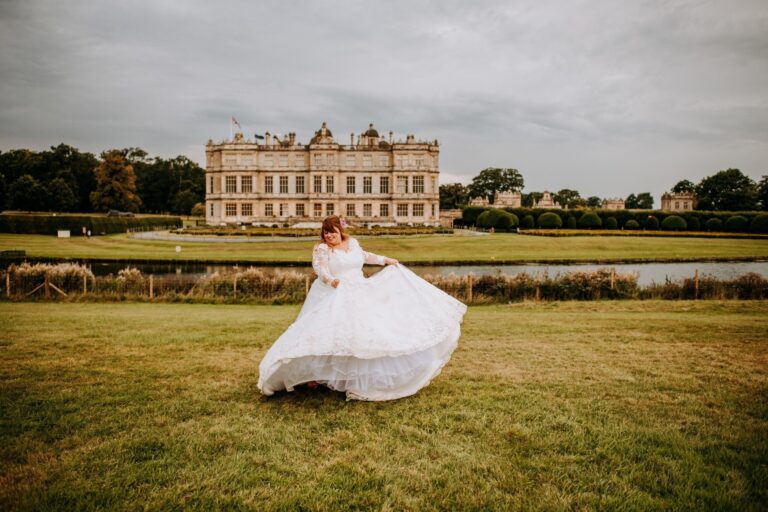 A bride in a full tulle skirt lifting the hem on the lawn before a large stately house, Catherine Blades Couture