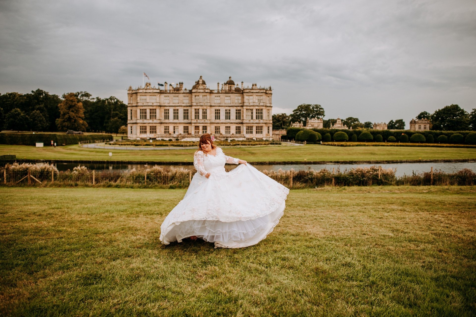 A bride in a full tulle skirt lifting the hem on the lawn before a large stately house, Catherine Blades Couture