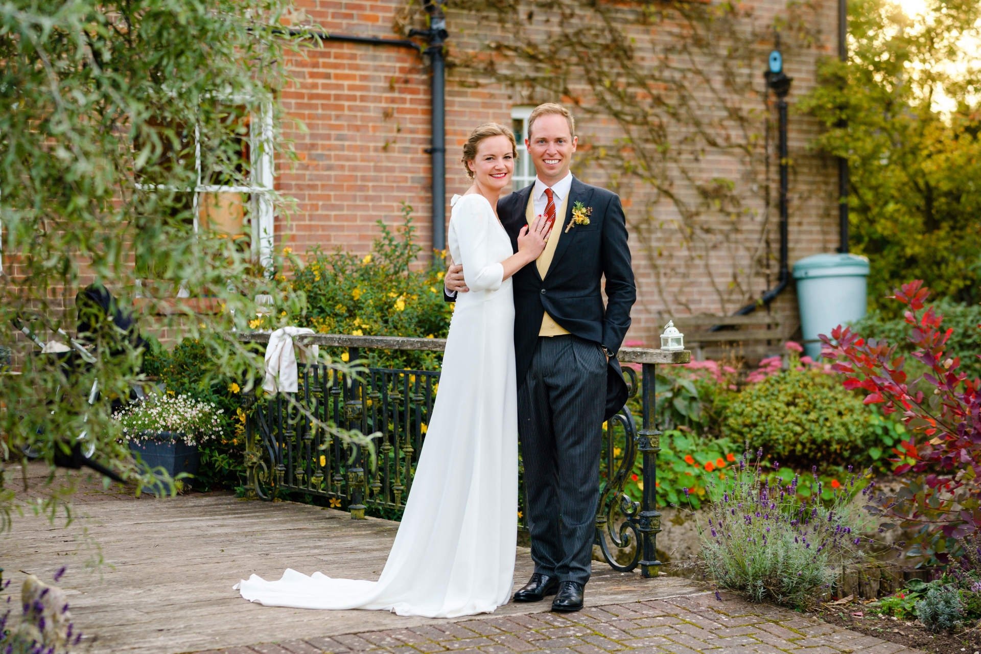 A couple on a brick terrace, the bride in a long-sleeved fitted ivory gown with a trailing hem, Catherine Blades Couture
