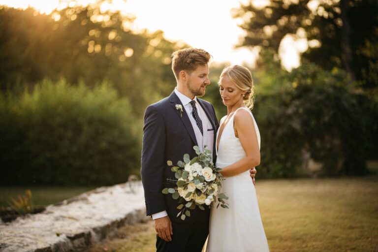 A couple at golden hour, the bride in a simple fitted gown holding a white bouquet, Catherine Blades Couture