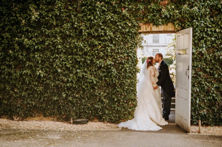 A couple at an open door in an ivy-covered wall, the bride in a lace gown with a long train, Catherine Blades Couture