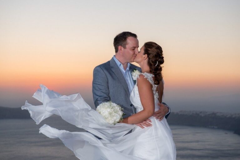 A couple kissing at sunset, the bride in a lace gown with a veil lifting in the wind, Catherine Blades Couture