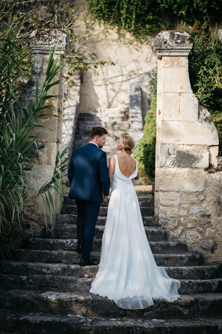 A bride in an open-back gown and a groom on old stone steps among ruins, Catherine Blades Couture