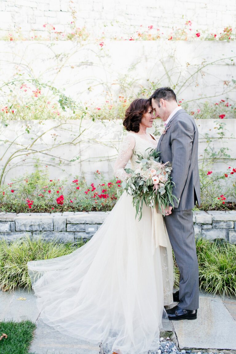 A couple in a walled rose garden, the bride in a gown with a long flowing train, Catherine Blades Couture