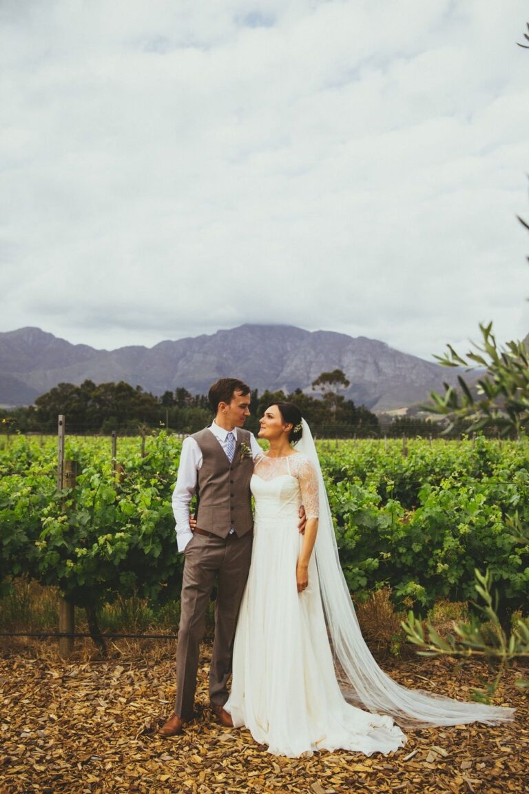 A couple in a vineyard beneath mountains, the bride in an ivory gown with a long veil, Catherine Blades Couture