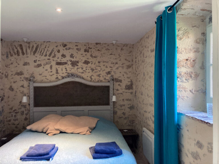 Bedroom with stone walls and a blue curtain, Château de Chéronne