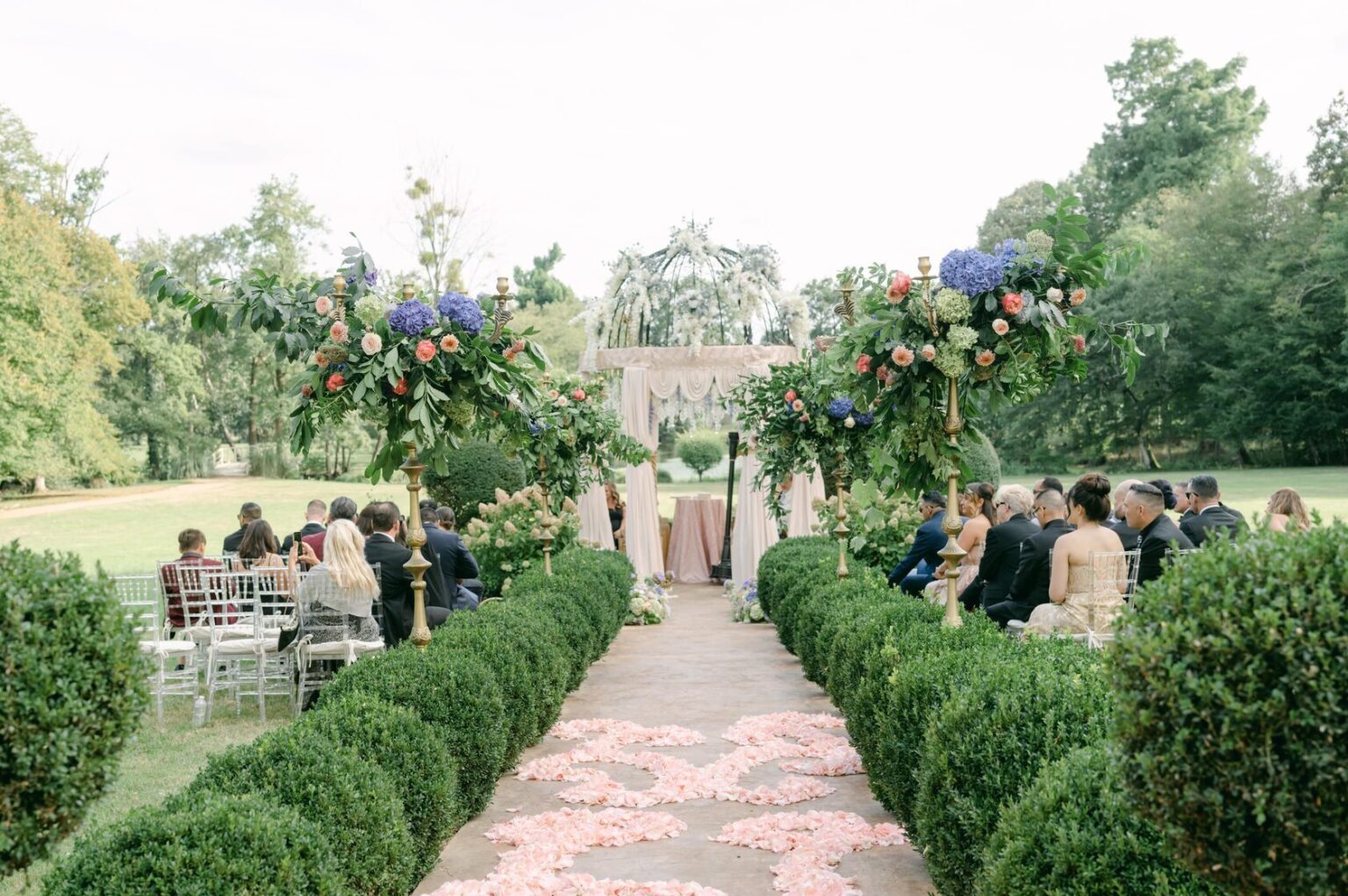 A garden ceremony along a hedge-lined aisle