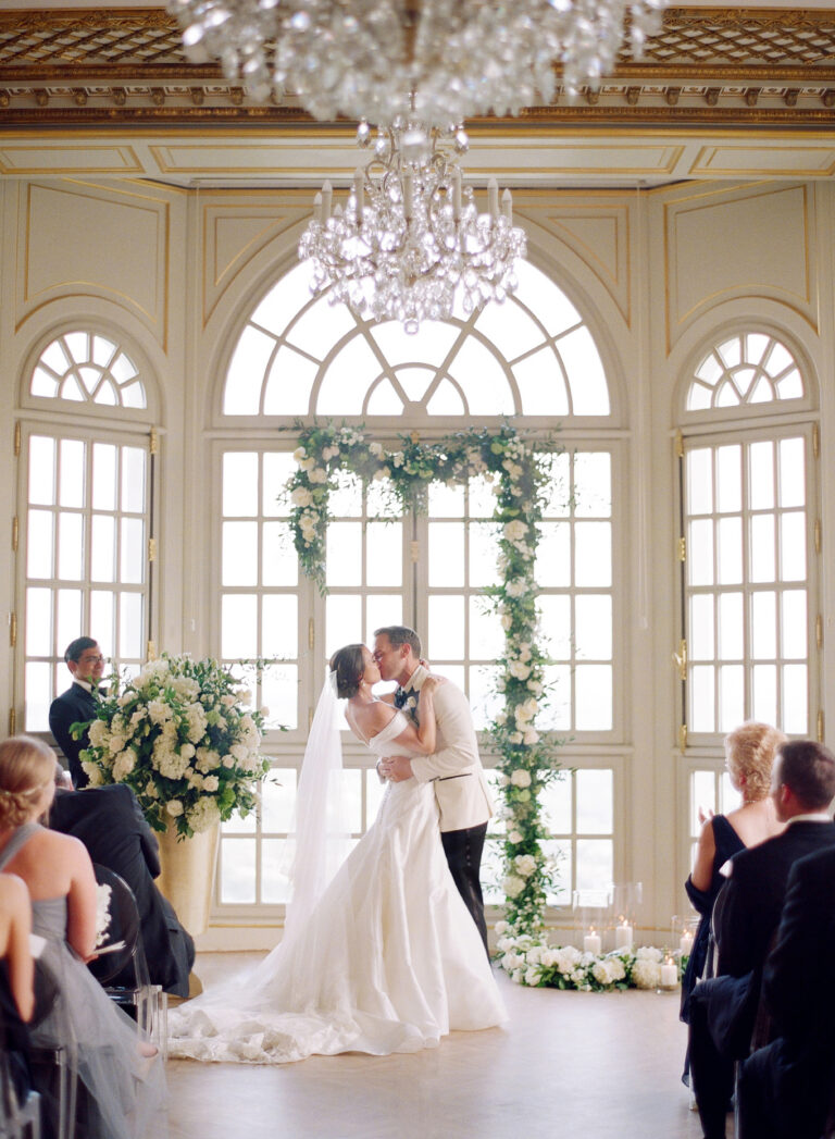 An indoor ceremony beneath the arched windows and chandelier, Chateau Saint Georges