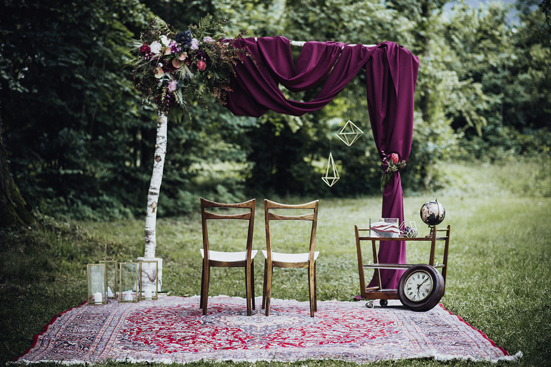 Ceremony arch of birch and plum drape over a patterned rug in a woodland clearing, Cherry On Top