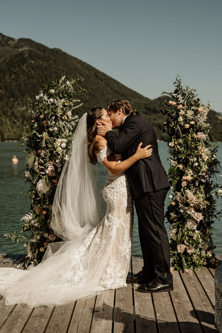 Couple kissing between tall floral arches on a lakeside jetty, Cherry On Top