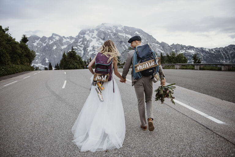 Couple with backpacks walking a mountain road, bride in a long gown, Cherry On Top