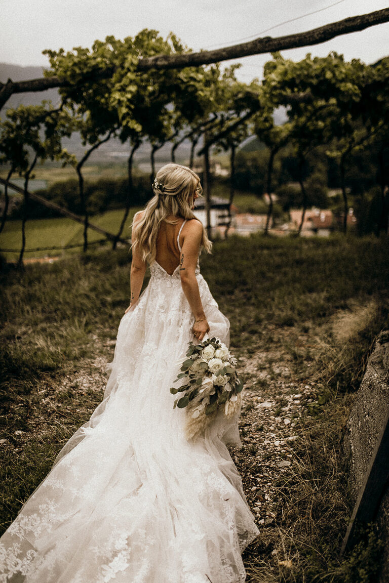 Bride seen from behind in a long lace gown among vines, Cherry On Top