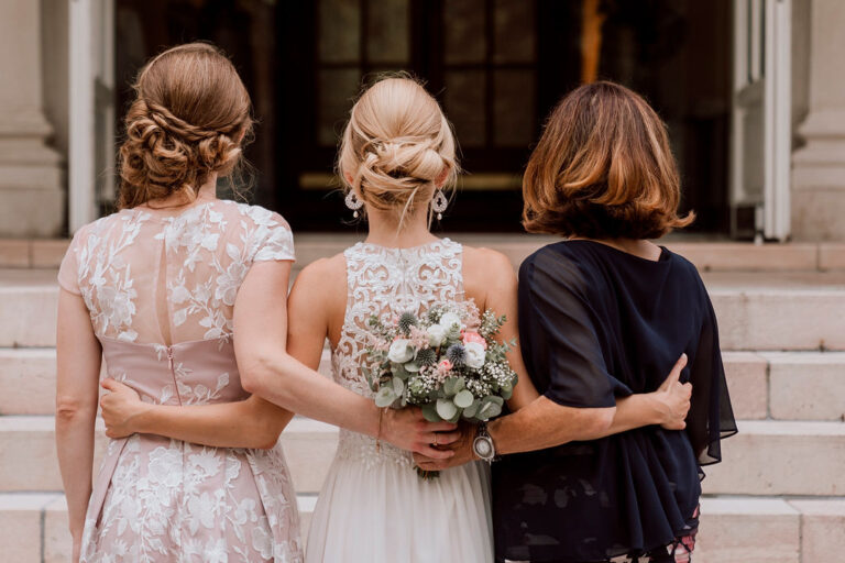 Bride with her mother and another guest, arms around each other, on stone steps, Cherry On Top