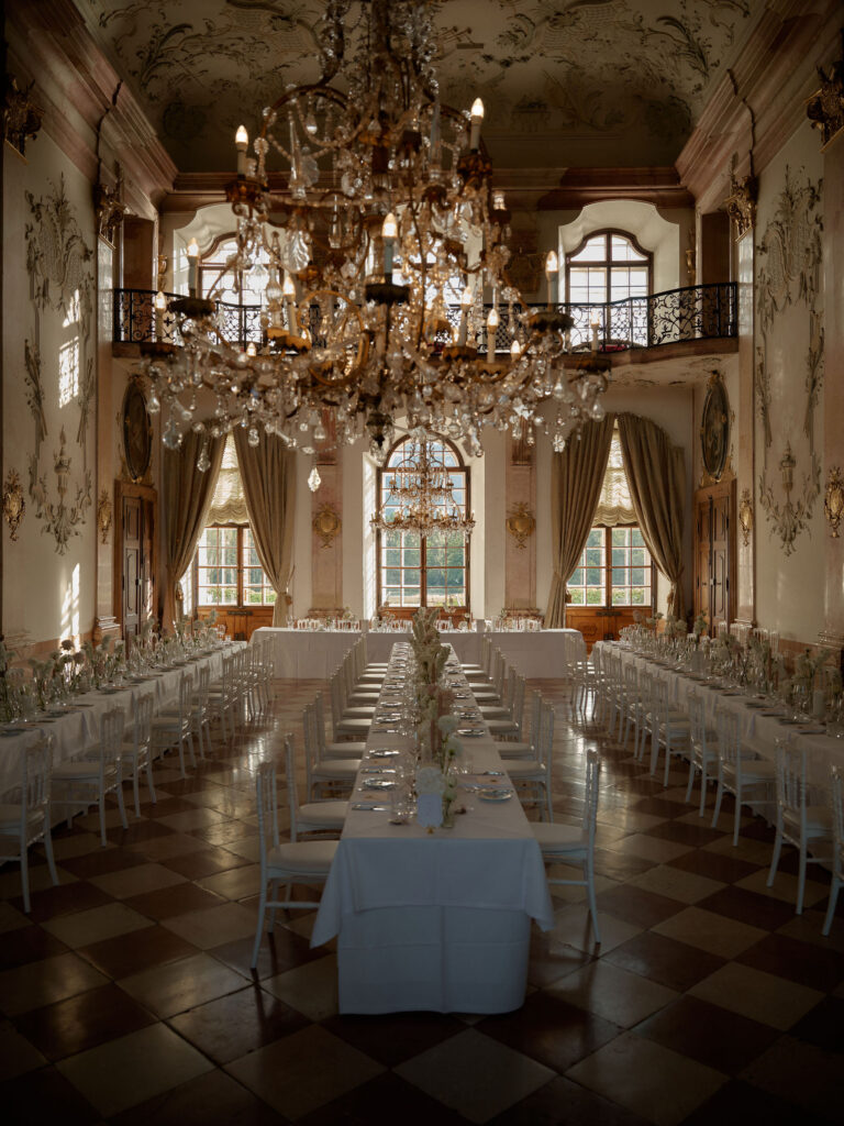 Long dinner tables beneath chandeliers in a grand hall, Cherry On Top