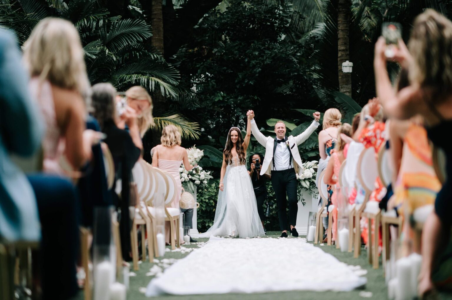 A couple raise their arms as they leave the aisle, guests on either side