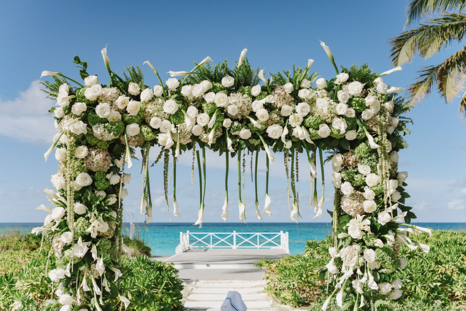 An arch of white roses and calla lilies frames a pier