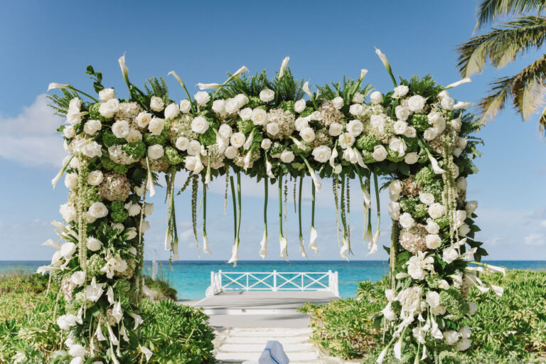 Floral arch of white roses and calla lilies framing a pier and turquoise water, Chic Bahamas Weddings