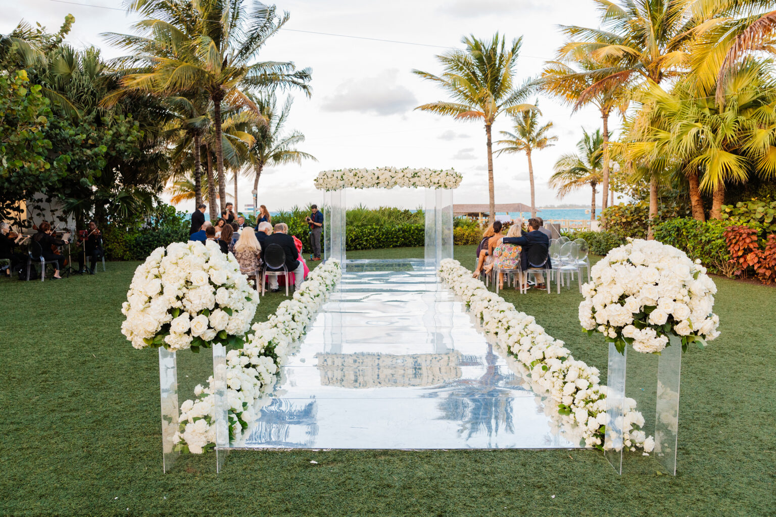 A mirrored aisle lined with white flowers leading to an acrylic canopy