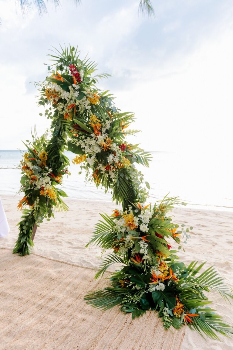 Asymmetric floral arch of tropical foliage and orange flowers on a beach, Chic Bahamas Weddings