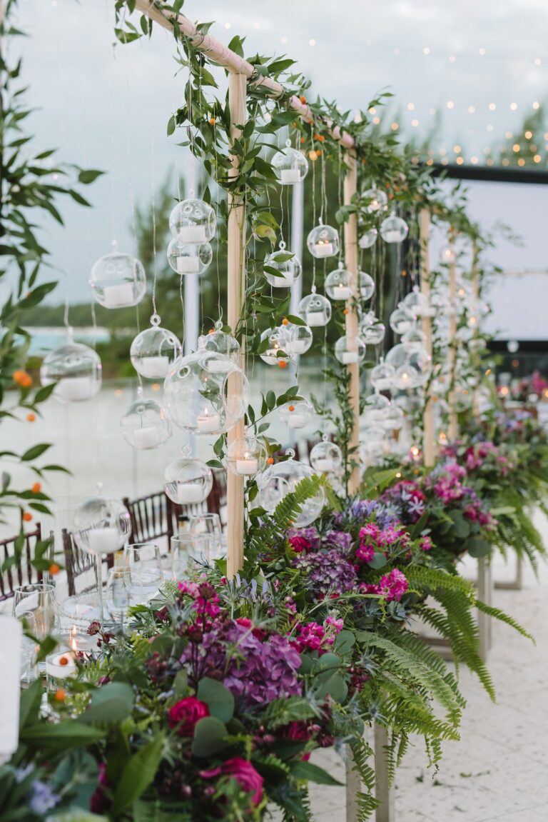 Hanging glass globes on a timber frame with bright flowers on a sandy beach, Chic Bahamas Weddings