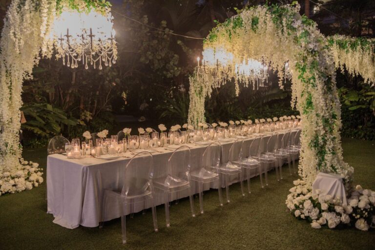 Long evening table beneath hanging wisteria and a floral arch with chandeliers, Chic Bahamas Weddings