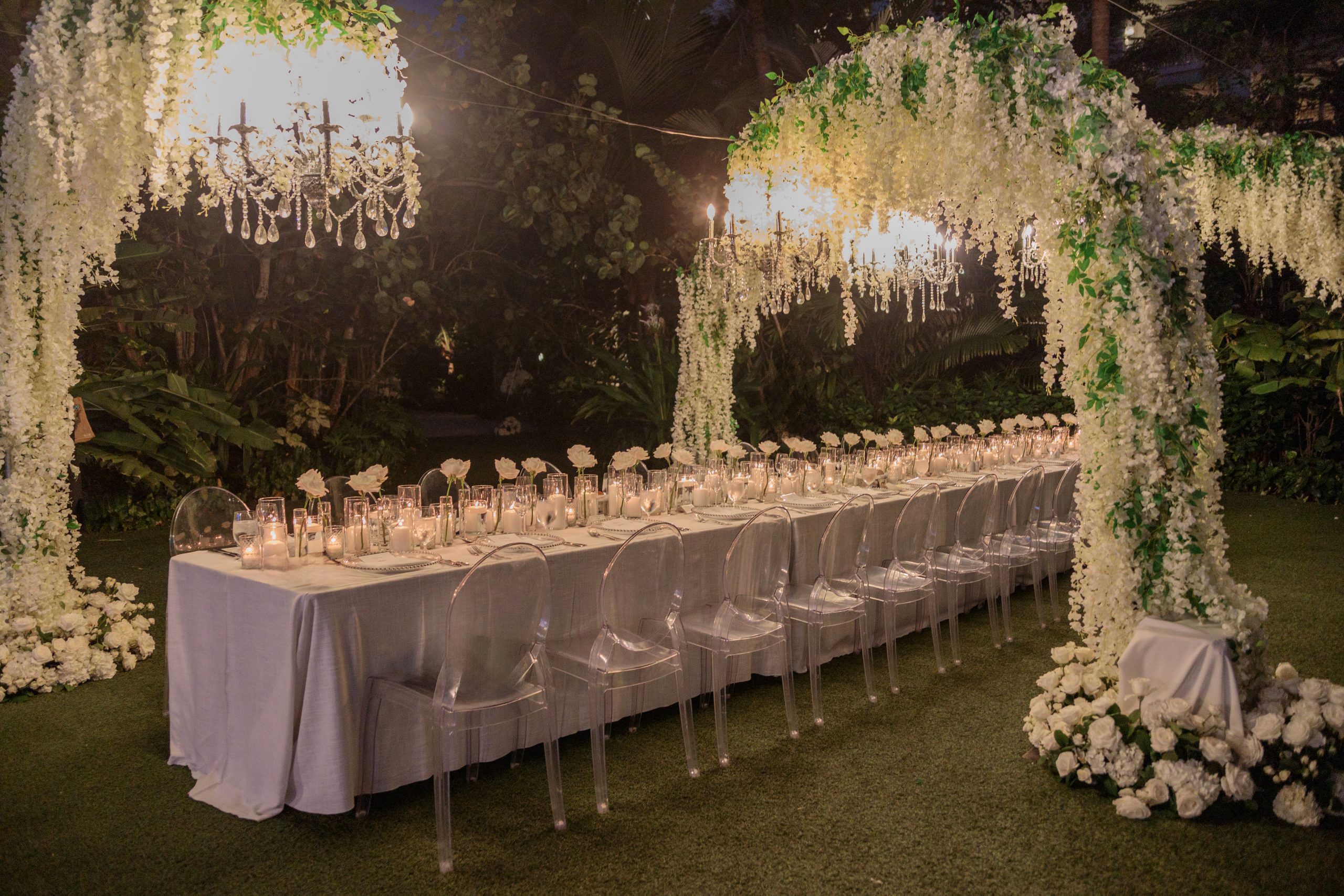 Long evening table beneath hanging wisteria and a floral arch with chandeliers, Chic Bahamas Weddings