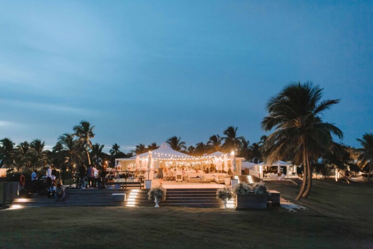 Reception tent lit up at dusk on a lawn with palms against a blue sky, Chic Bahamas Weddings