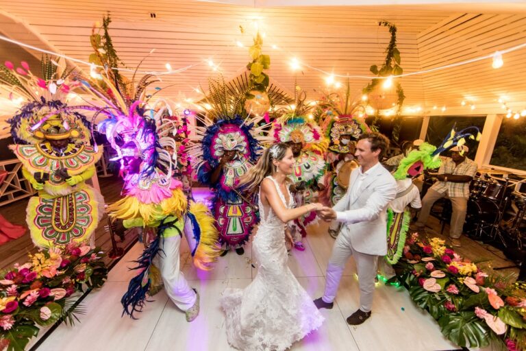 Couple dancing with Junkanoo costumed performers in a decorated pavilion, Chic Bahamas Weddings