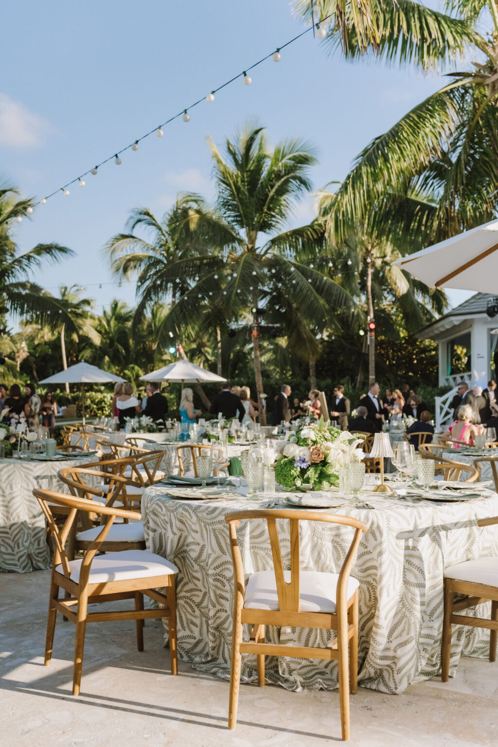 Round reception tables on a beachside terrace in the evening light, with palms, Chic Bahamas Weddings