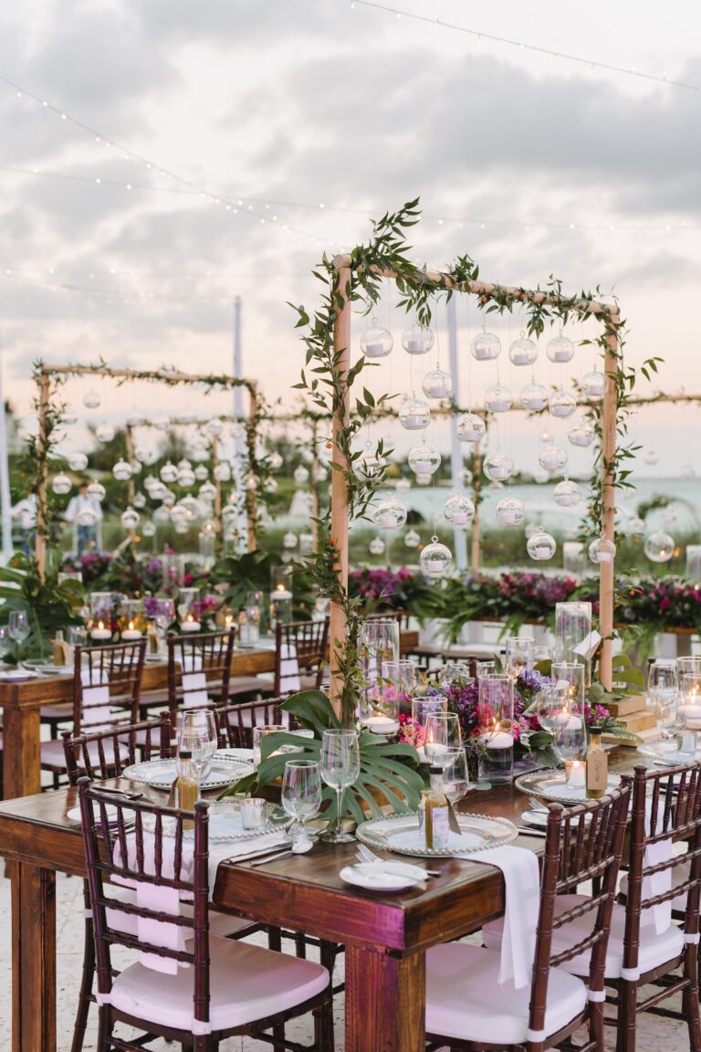 Dining tables beneath floral arches on a beach at sunset, Chic Bahamas Weddings