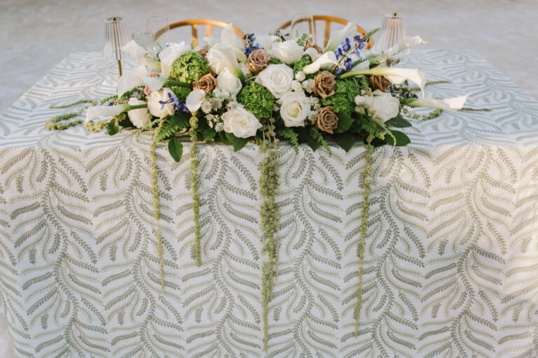 Sweetheart table dressed in a leaf-print cloth with a white floral arrangement, Chic Bahamas Weddings